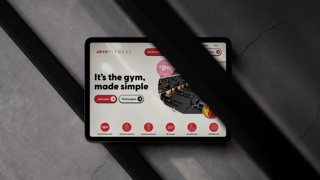 iPad mockup showing Revo Fitness app with 'It's the gym, made simple' tagline on a diagonal dark background
