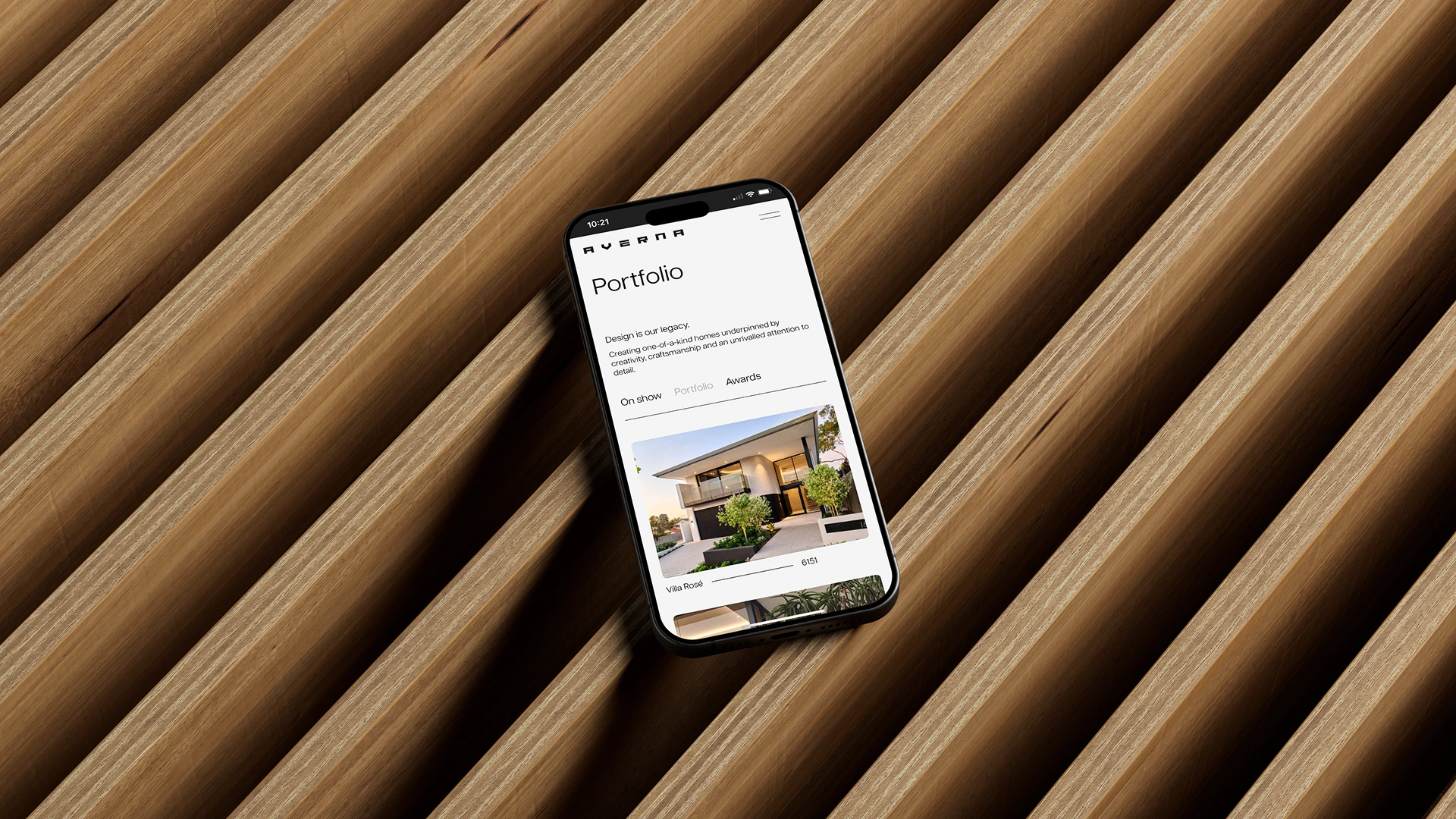 Hand holding a smartphone showing the Averna Homes website, in front of diagonal timber slats