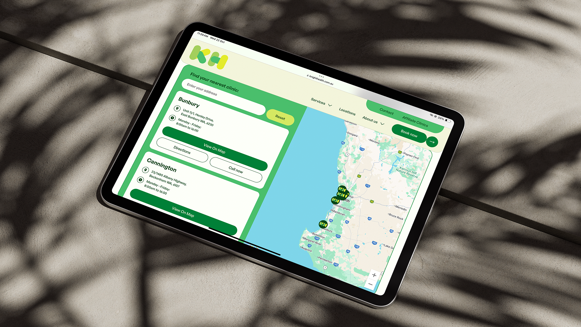 Tablet showing a green map-based web interface, on a surface with palm leaf shadows