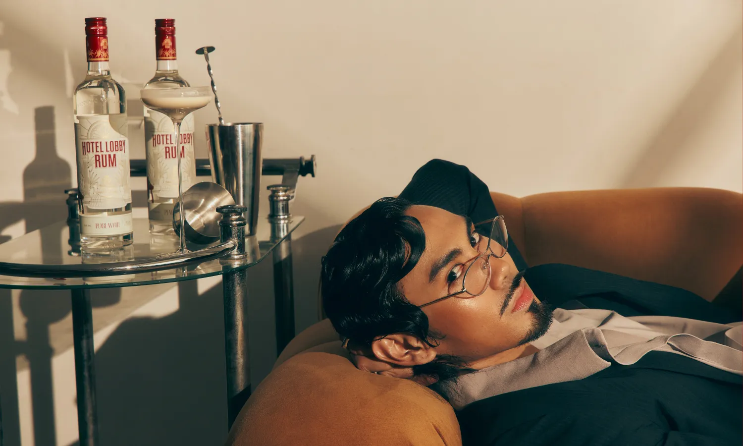 Hotel Lobby Rum lifestyle — man in dark suit reclining in an elegant bar setting with rum bottles