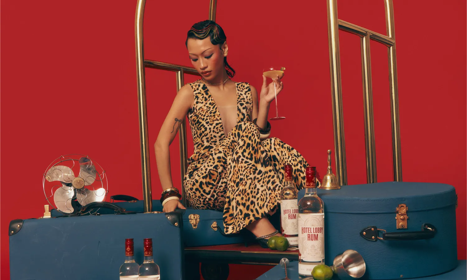 Hotel Lobby Rum lifestyle image — woman in leopard print dress with vintage luggage on red background