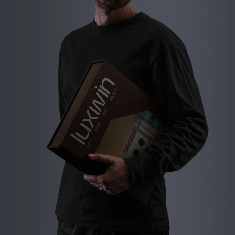 A person in dark clothing holding a Luxwin branded box or product against a dark background — luxury brand photography