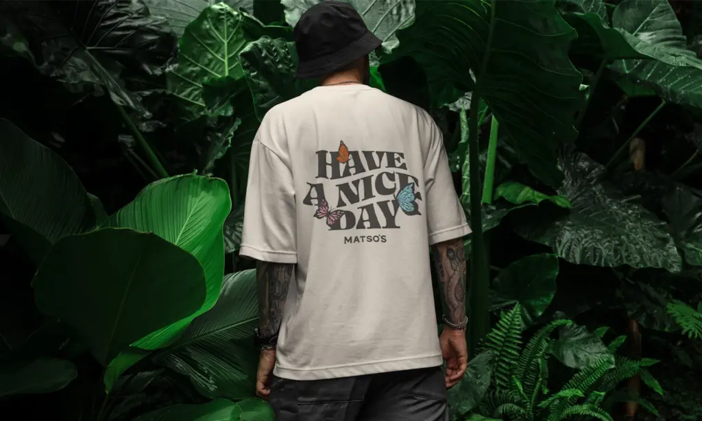 Person wearing a white t-shirt from behind showing a printed slogan design in a lush tropical jungle setting