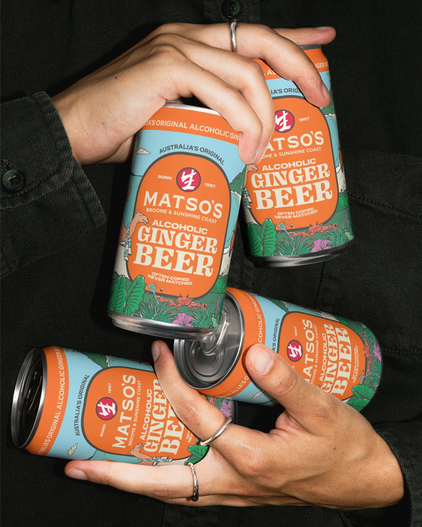 Multiple hands raising Matso's Brewery beer cans in an overhead shot showing orange branded packaging