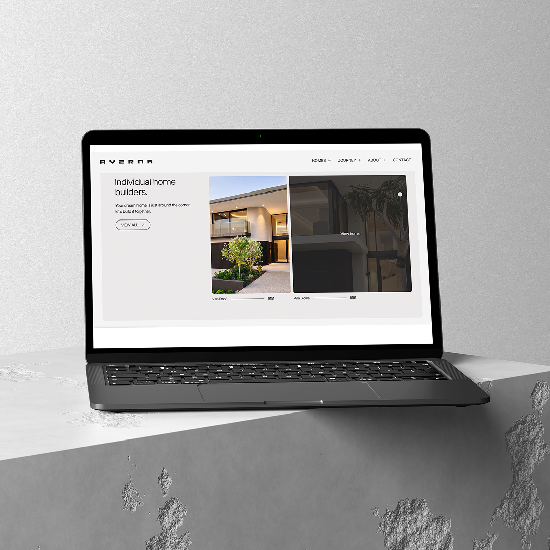 White MacBook laptop showing a website design on a minimal light grey background