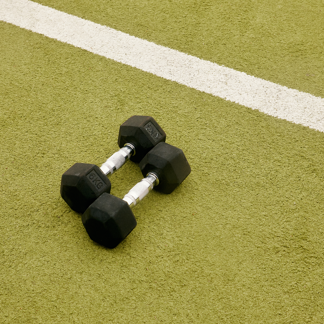 Two black dumbbells resting on a green gym mat surface