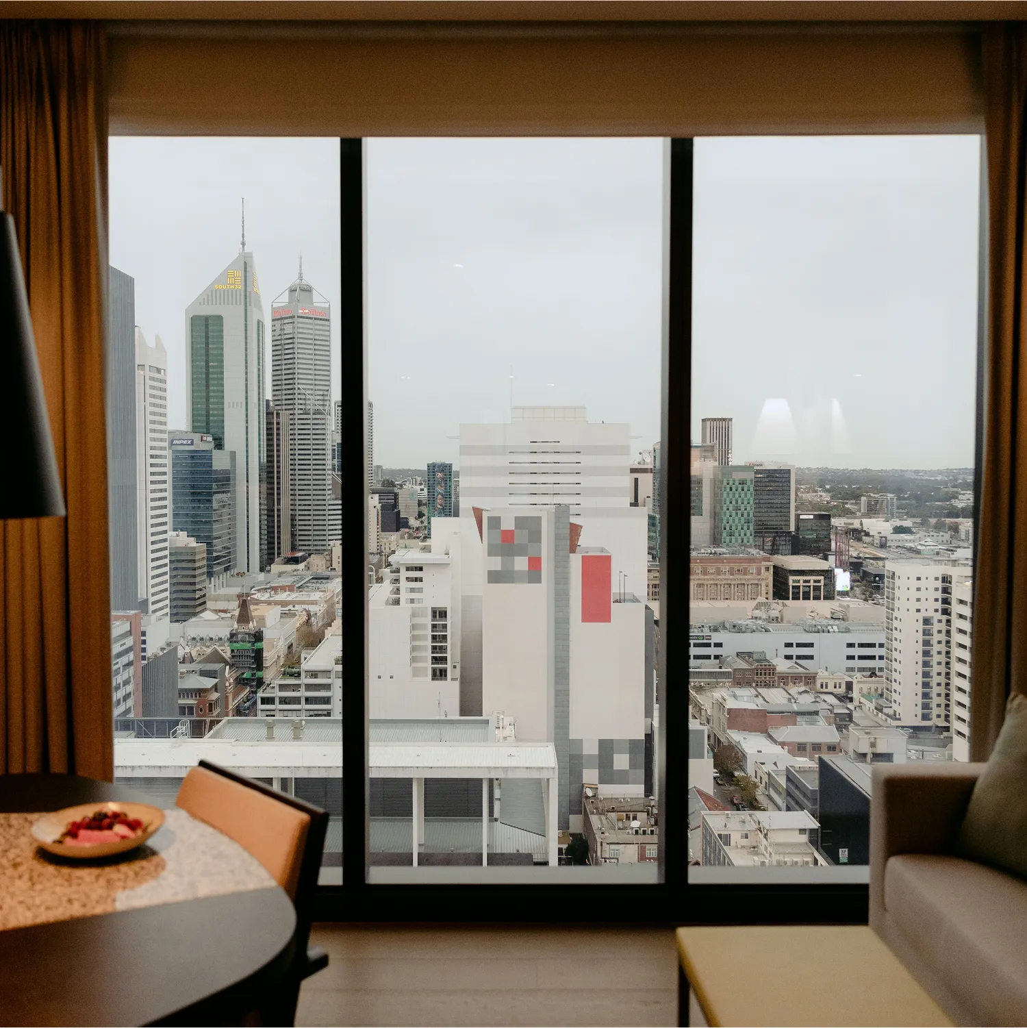 Luxury hotel room interior with floor-to-ceiling windows overlooking a city skyline at dusk