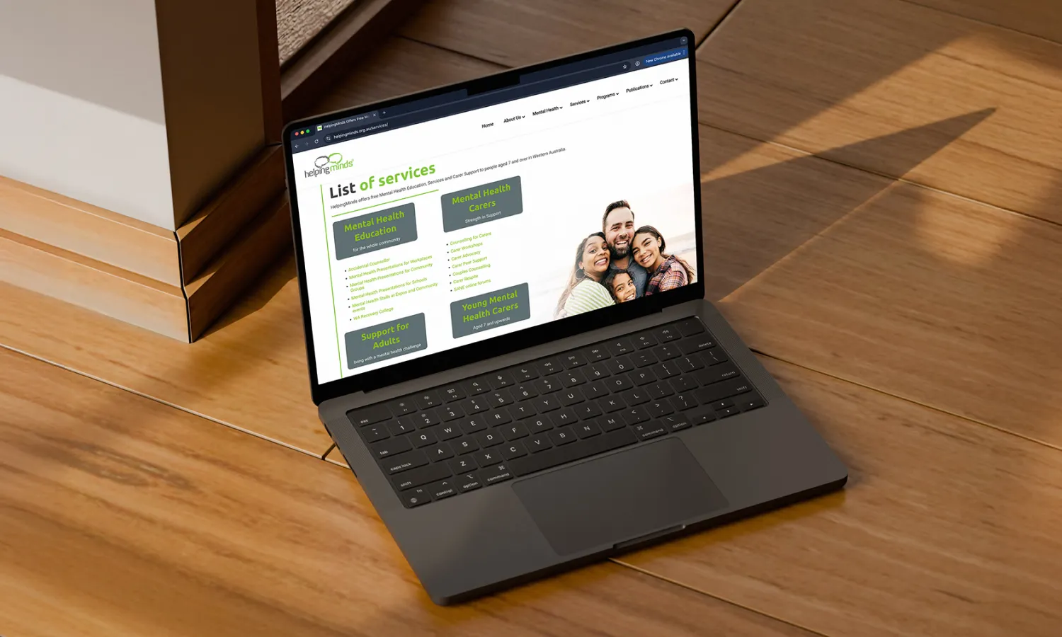 MacBook laptop on a wooden surface showing the HelpingMinds website design