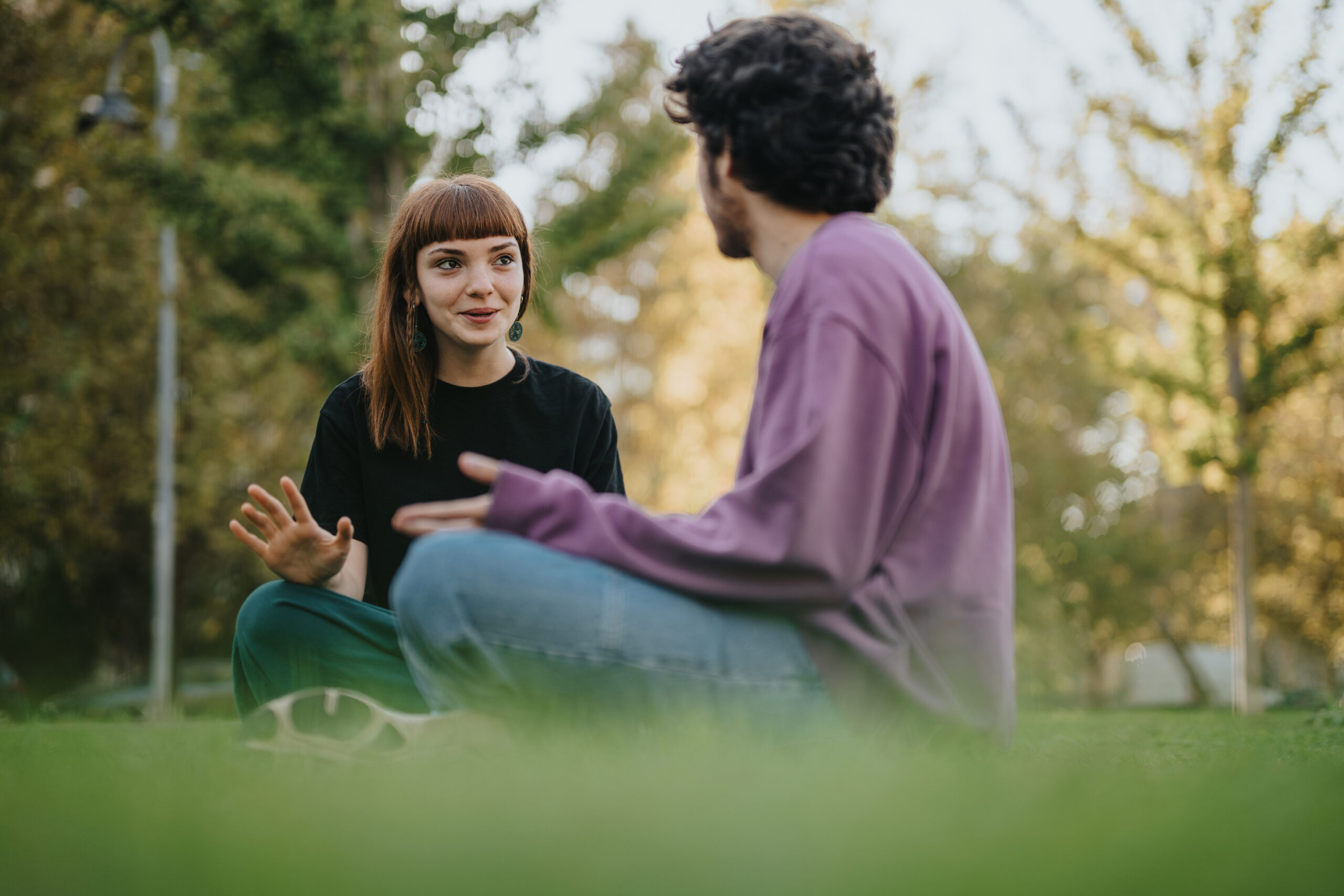 Two young people sitting on grass in bright sunlight having a conversation — HelpingMinds campaign