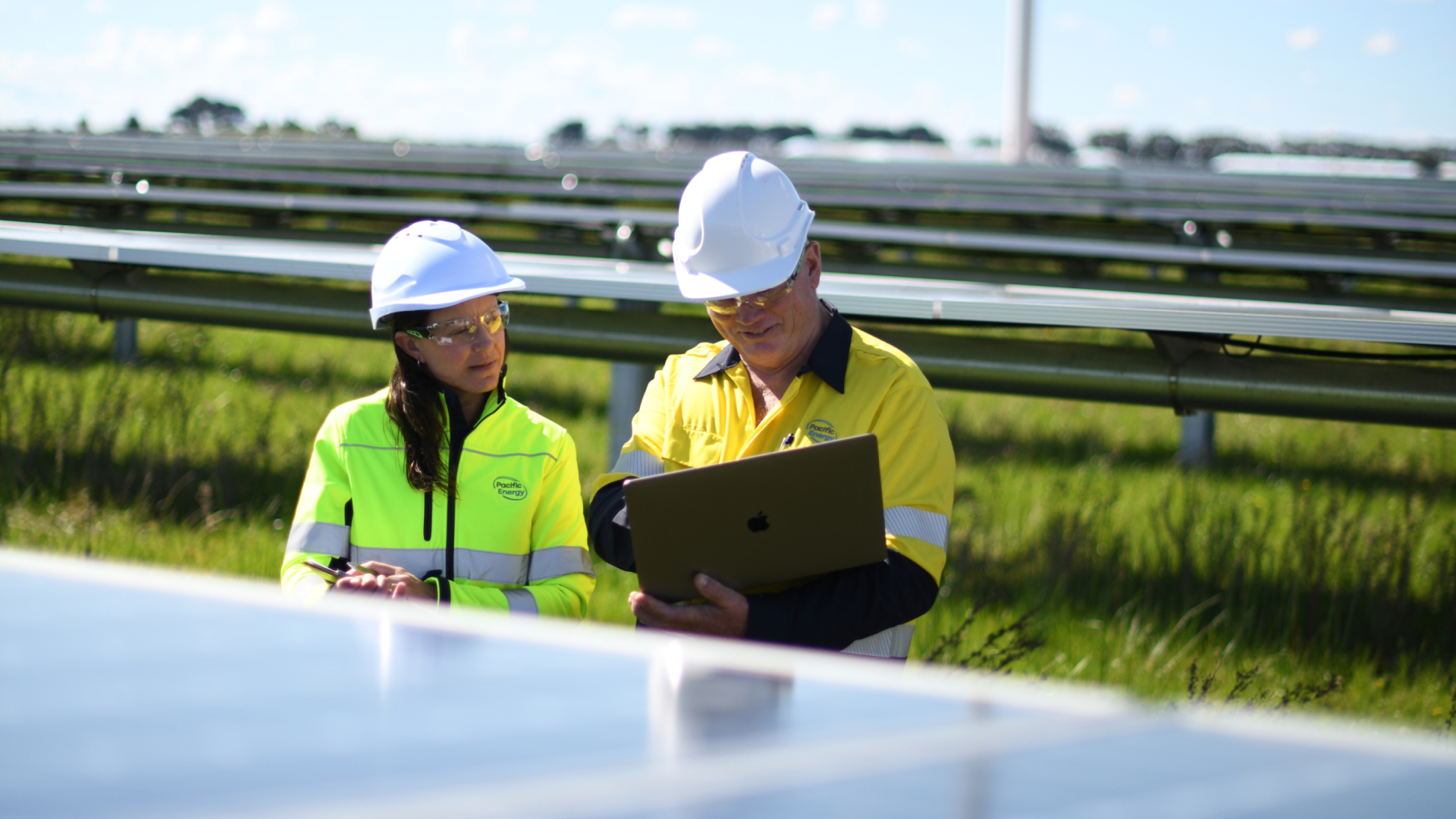 Two workers in yellow hi-vis jackets working beside solar panels in bright sunshine