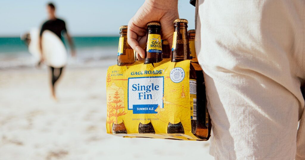 Multiple Single Fin beer bottles held up against a bright beach and ocean background