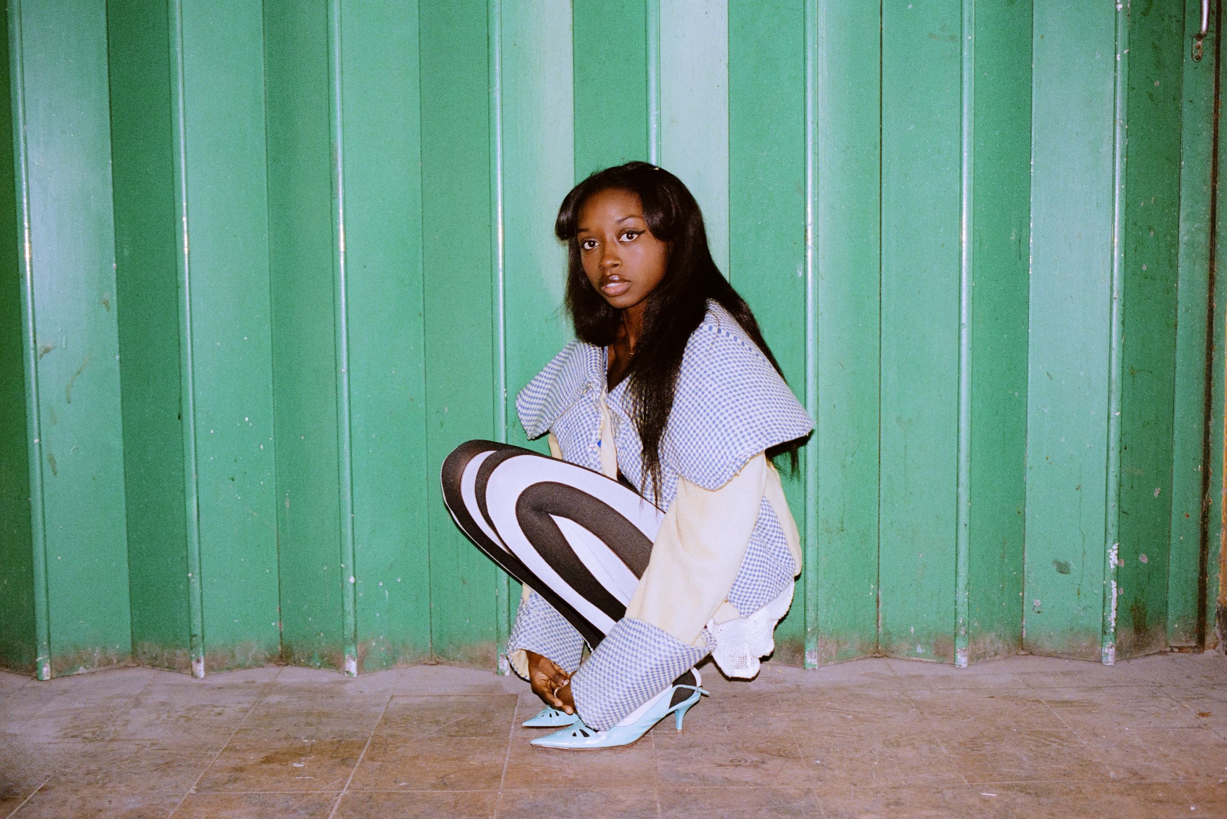Young woman in an oversized white outfit posed against a green corrugated metal wall