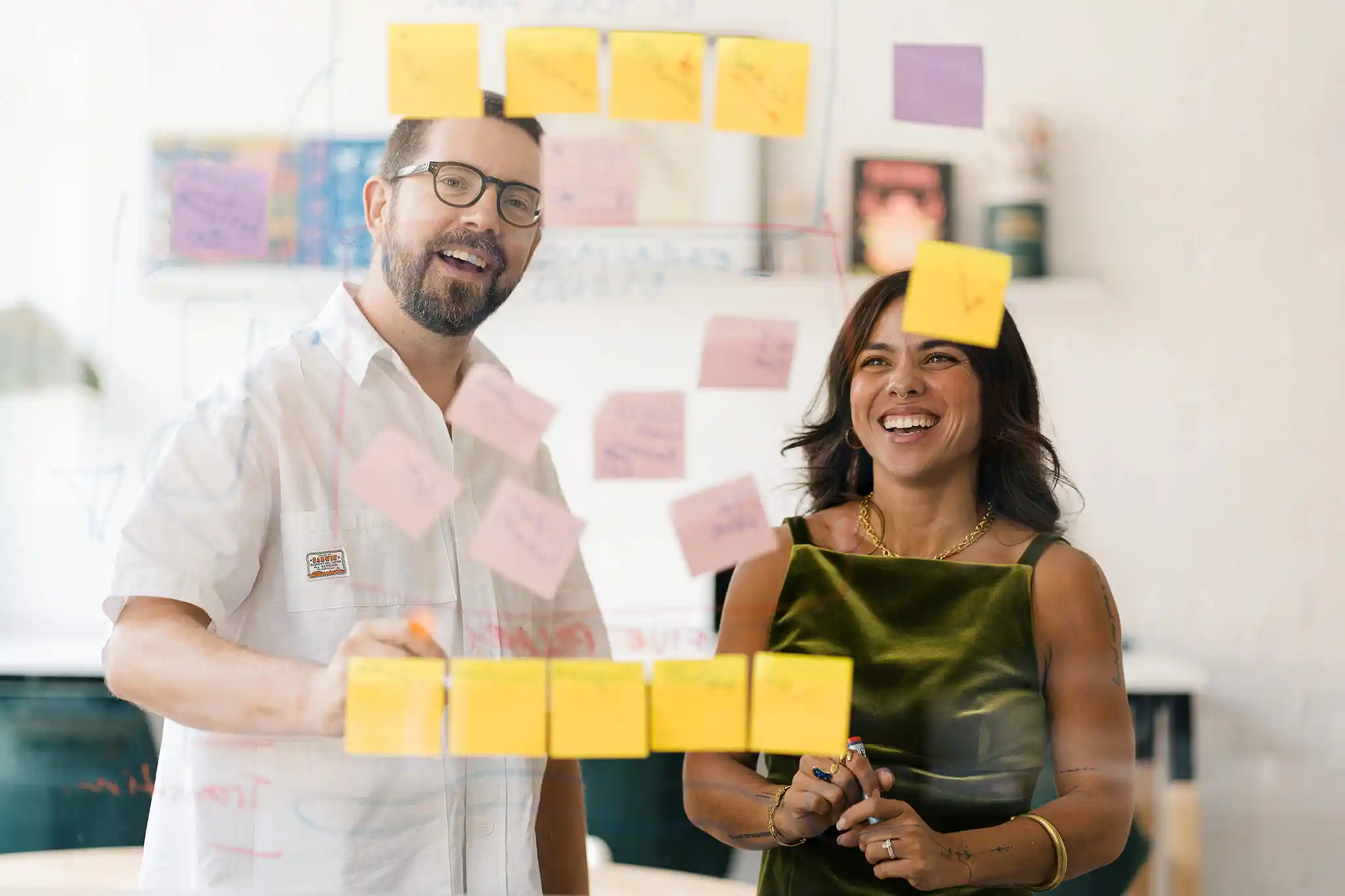 Two Start team members in a brainstorm workshop session with papers and sticky notes on the wall, both smiling